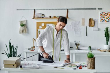 Genç bir adam DIY giysi restorasyon atölyesinde bir kumaş parçasını dikkatlice ütülüyor, sürdürülebilirliğe odaklanıyor ve atılmış giysileri canlandırıyor..