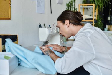 Beyaz gömlekli genç bir adam titizlikle dikiş makinesine odaklanıyor atölyesindeki atölye kıyafetlerini restore ediyor, sürdürülebilir modaya olan bağlılığının bir kanıtı..