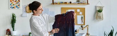 A young man, dressed in a white shirt, examines a restored garment in his DIY clothing restoration atelier, emphasizing sustainable practices. clipart