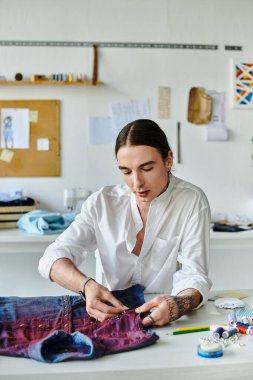 Genç bir adam, sürdürülebilir giysi restorasyon atölyesindeki eski bir kot gömleği titizlikle onarıyor..