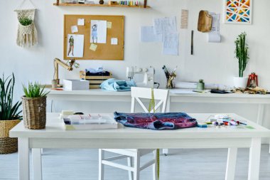 A white table in a brightly lit atelier, showcasing a denim garment ready for upcycling. clipart