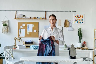 A young man in a white shirt works on a garment in his clothing restoration atelier, emphasizing sustainability and giving new life to old items. clipart