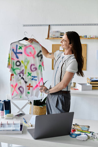 A young man in a DIY clothing restoration atelier proudly displays a vibrant, upcycled t-shirt.