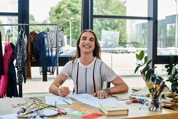 A young man smiles as he sketches designs for his clothing restoration atelier. Hes surrounded by discarded garments ready for a second life.