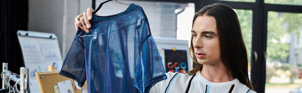 A young man, focused intently, holds up a delicate, blue, mesh garment, highlighting his passion for reviving old clothing and promoting sustainable fashion practices.