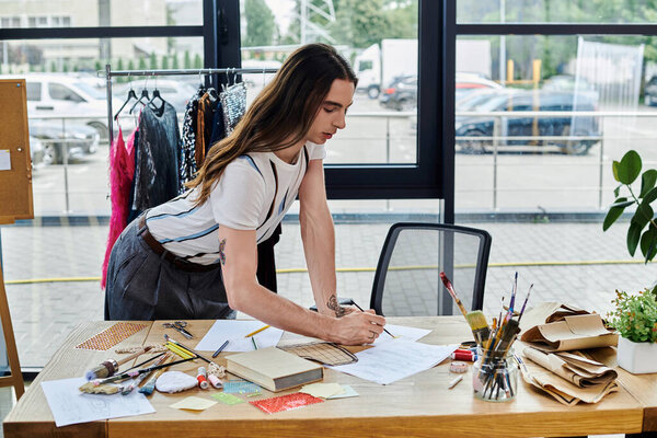 A young man works on a design in his clothing restoration atelier, surrounded by tools and materials for his sustainable fashion endeavors.