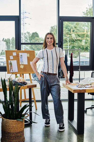 A young man stands in his atelier, surrounded by his work, showcasing his passion for sustainable clothing restoration.