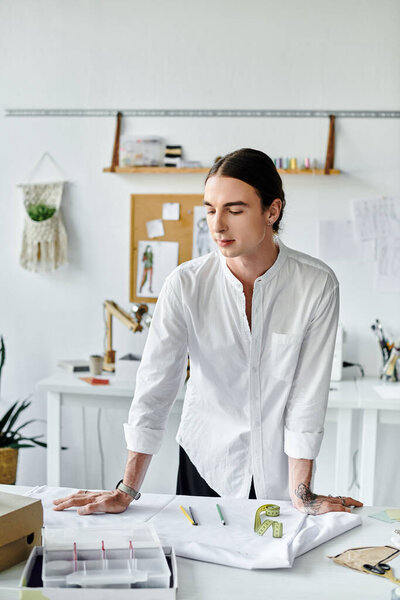 Молодой человек в белой рубашке стоит в ателье реставрации одежды, сосредоточенный на своей работе.