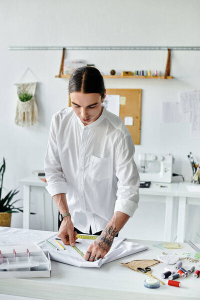 A young man in a white shirt measures fabric with a tape measure, meticulously working on a new clothing project in his sustainable atelier.