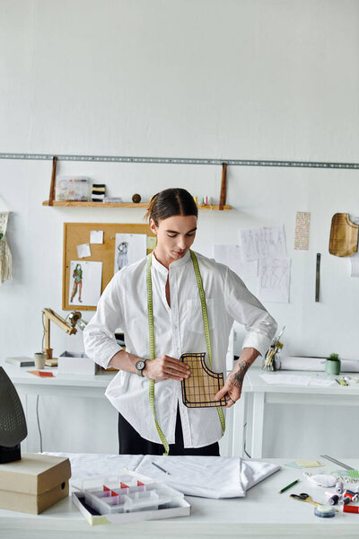 A young tailor in a white shirt meticulously examines a pattern piece in his clothing restoration atelier.