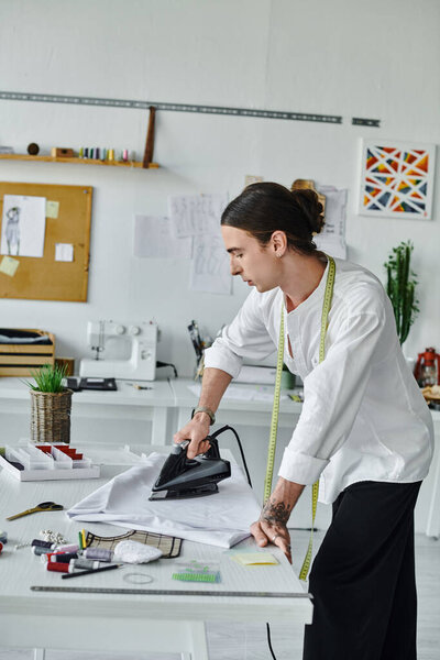 Молодой портной в белой рубашке гладит одежду в ателье, демонстрируя свою страсть к устойчивому восстановлению одежды.