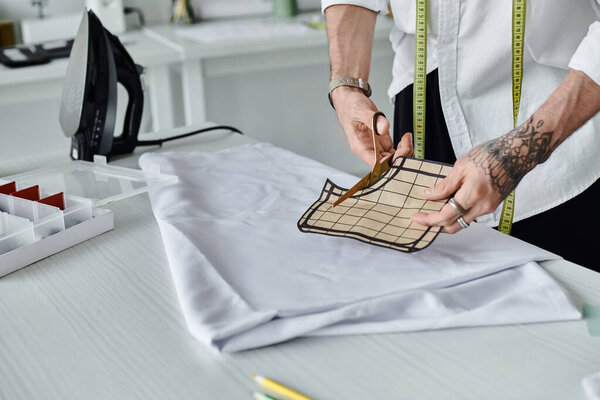 A young man, wearing a white shirt and a measuring tape, cuts fabric in his atelier. He is focused on sustainability and reviving old clothing.