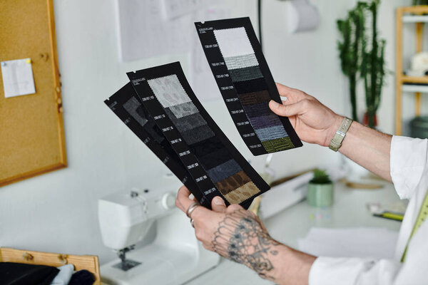 A young man in a white shirt examines fabric swatches in his clothing restoration atelier.