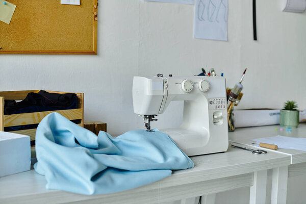 Белая швейная машинка сидит готовая к действию на чистое белое рабочее место. Кусок синей ткани лежит на столе, готовый к новой жизни через искусство реставрации одежды.