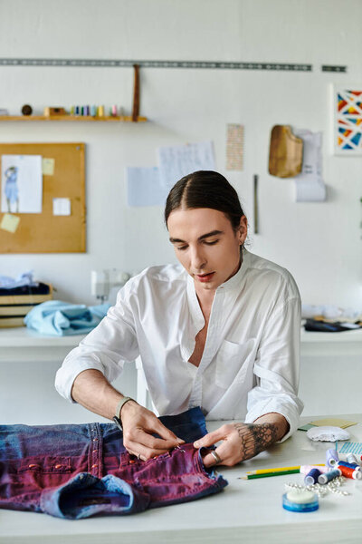 Молодой человек тщательно ремонтирует винтажную джинсовую рубашку в своей мастерской по восстановлению одежды..