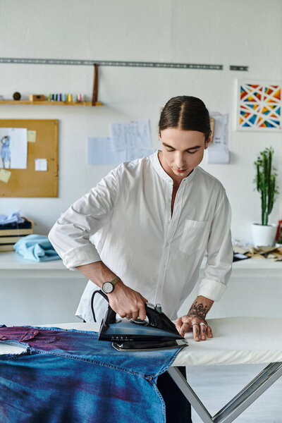 A young man meticulously irons a pair of denim jeans in his clothing restoration atelier.
