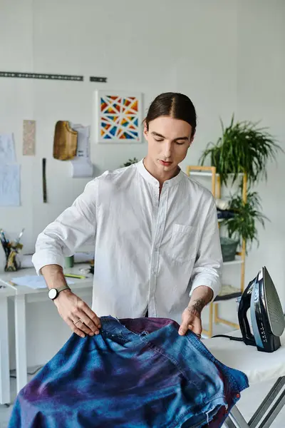 stock image A young man in a white shirt meticulously irons a vintage denim garment, breathing new life into it within his DIY clothing restoration atelier.