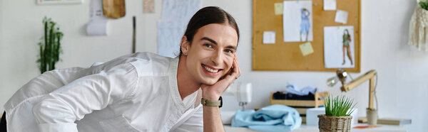 A young man in a white shirt smiles brightly as he works in his clothing restoration atelier.