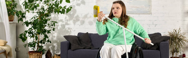 A young brunette woman in a wheelchair sits in her living room, holding a broom in her hands.