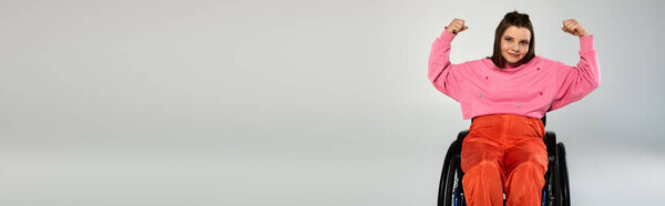 Молодая женщина с каштановыми волосами, в повседневной одежде, сидит в инвалидном кресле и сгибает бицепсы в студии.