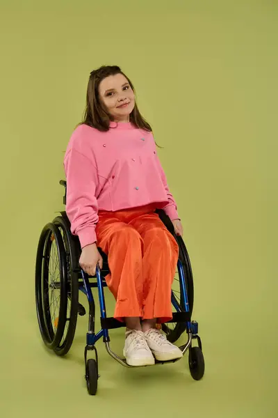 stock image A young woman with a disability, in a wheelchair, confidently poses for a picture in a studio wearing casual attire.