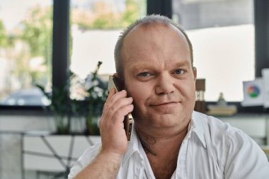 Kapsamlı bir adam modern bir ofiste masa başında oturup telefonuyla konuşur..