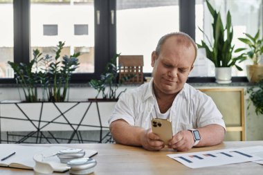 Kapsamlı bir adam modern bir ofiste masa başında oturmuş, akıllı telefonunu kontrol ediyor..
