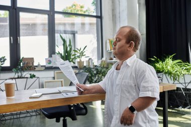 Beyaz gömlekli bir adam modern bir ofiste masa başında bir belgeyi inceliyor..