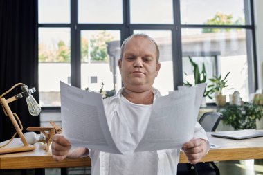 Kapsamlı bir adam iyi aydınlatılmış bir ofiste masa başında oturmuş belgeleri dikkatle inceliyor..