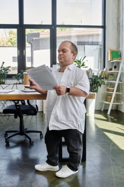 Kapsamlı bir adam bir ofis ortamında elinde bir fincan kahve tutarken belgelere bakıyor..