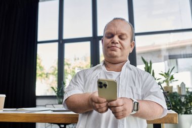 Kapsamlı bir adam modern ofis ortamında oturup telefonunu kontrol eder..
