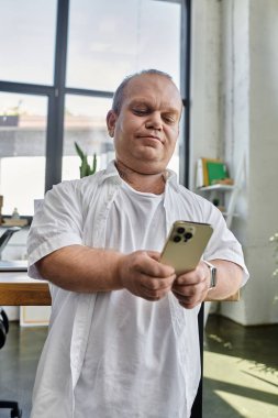 Kapsamlı bir adam ofis ortamında telefonuna bakar..