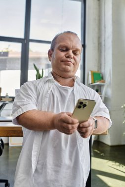 A man with inclusivity looks at his phone in an office setting. clipart