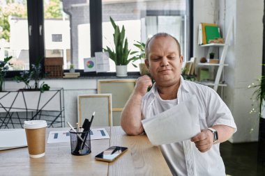 A man with inclusivity sits at a desk in his office, reviewing documents with a cup of coffee. clipart