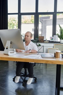 Kapsayıcılığı olan bir adam modern bir ofiste masasında oturmuş bilgisayarını tamir ediyor..