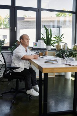 Kapsayıcılığı olan bir adam modern bir ofiste masa başında oturuyor ve bir proje üzerinde çalışıyor..