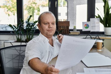 Kapsamlı bir adam modern bir ofiste masasında oturmuş, düşünceli bir şekilde belgeleri inceliyor..