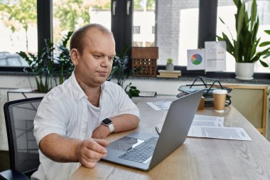 Kapsamlı bir adam ofisinde masasında oturup dizüstü bilgisayarıyla çalışır..