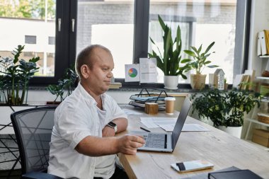 Kapsayıcılığı olan bir adam laptopuyla modern bir ofis alanında çalışır..