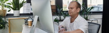 A man with inclusivity is working on a computer in a well-lit office space. clipart