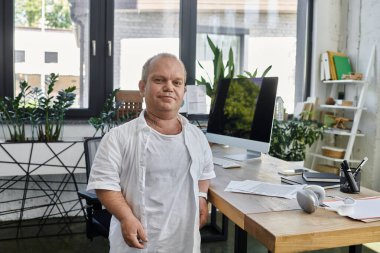 Kapsayıcılığı olan bir adam, işyerinde çeşitliliğin ve kapsayıcılığın önemini göstererek, kendinden emin bir şekilde ofisinde duruyor..