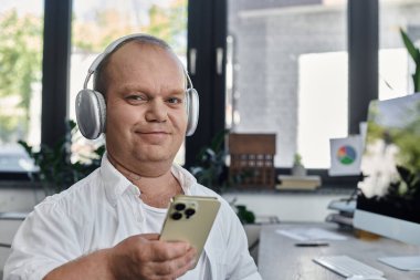 Kapsayıcı kulaklık takan bir adam ofisinde masasında oturuyor..