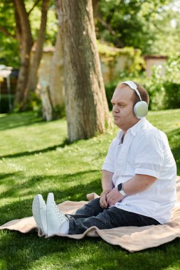 Kapsayıcı bir adam parkta bir battaniyeye oturur, kulaklık takar ve müzik dinler..