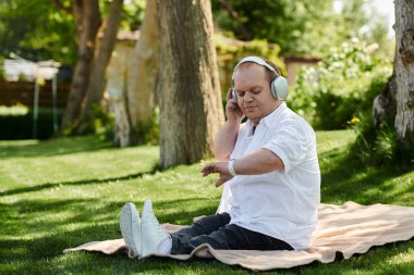 Kapsamlı bir adam parkta bir battaniyeye oturmuş, kulaklık takıyor ve akıllı bir şey takıyor..