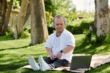 Kapsayıcı bir adam parkta bir battaniyeye oturur, kulaklık takar ve müzik dinler..