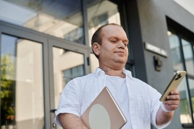 Kapsamlı bir adam modern bir ofis binasının önünde akıllı telefonunu kullanarak yürür..