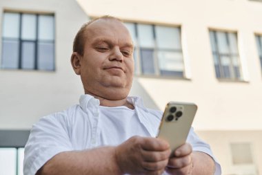 Beyaz tişörtlü bir adam şehirde yürürken akıllı telefon kullanır..