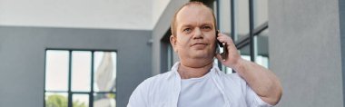 Beyaz tişörtlü bir adam dışarıda telefonuyla yürüyor ve konuşuyor..