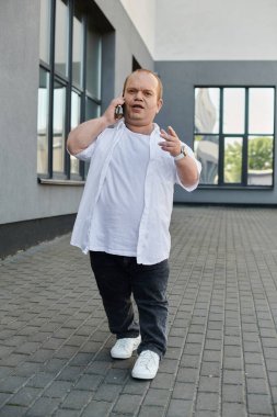 Beyaz gömlekli bir adam telefonuyla yürüyor ve konuşuyor, gülümsüyor..