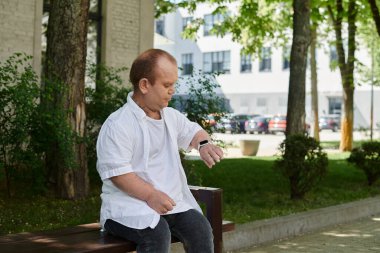 Kapsamlı bir adam, güneşli bir günde parkta bir bankta oturur ve saatini kontrol eder..